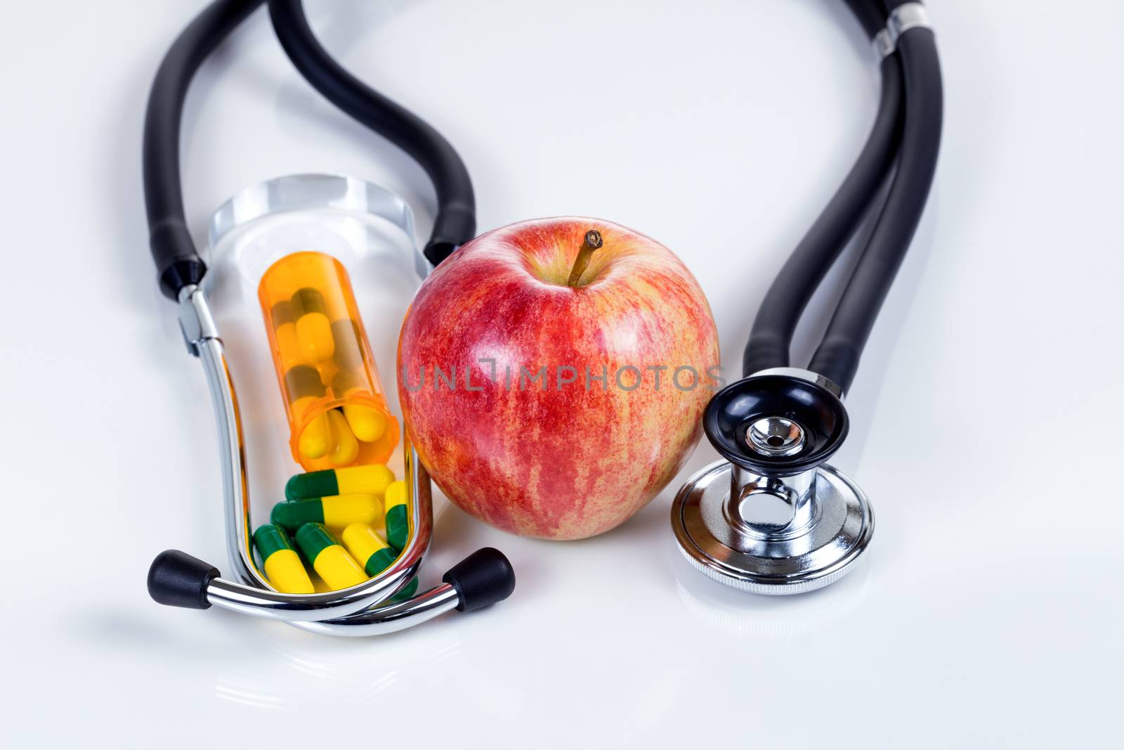 Red apple, medicine capsules and stethoscope on white table with reflection. Good health care concept. 