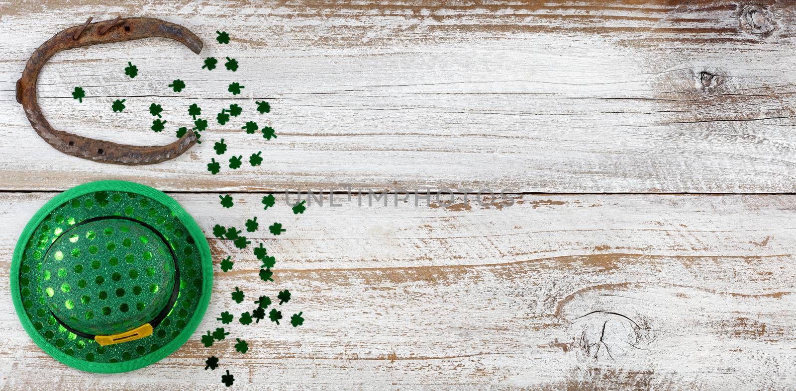 St Patricks day good luck hat and horseshoe with shiny clovers forming border on left side of rustic white wooden boards