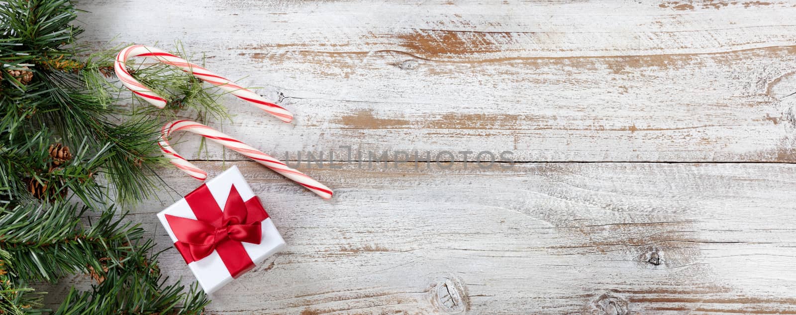Rough fir branches with Christmas gift box and candy canes on rustic white wooden boards 