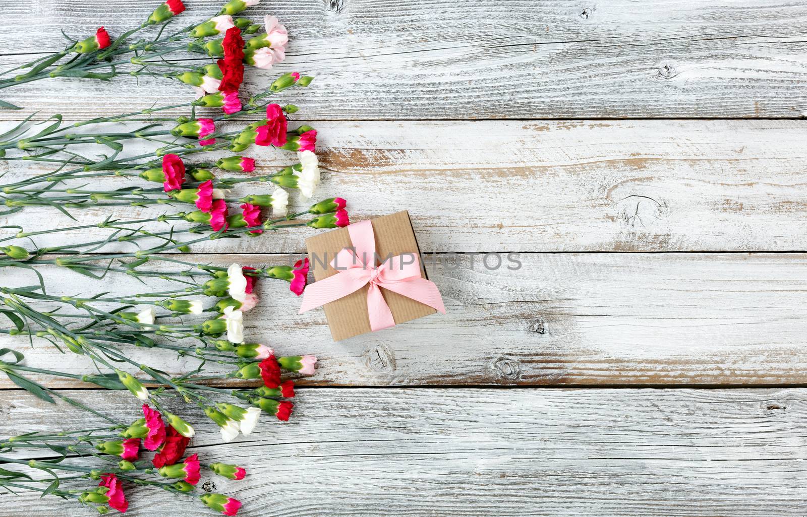 Colorful carnations and gift forming left border on white weathered wooden boards 
