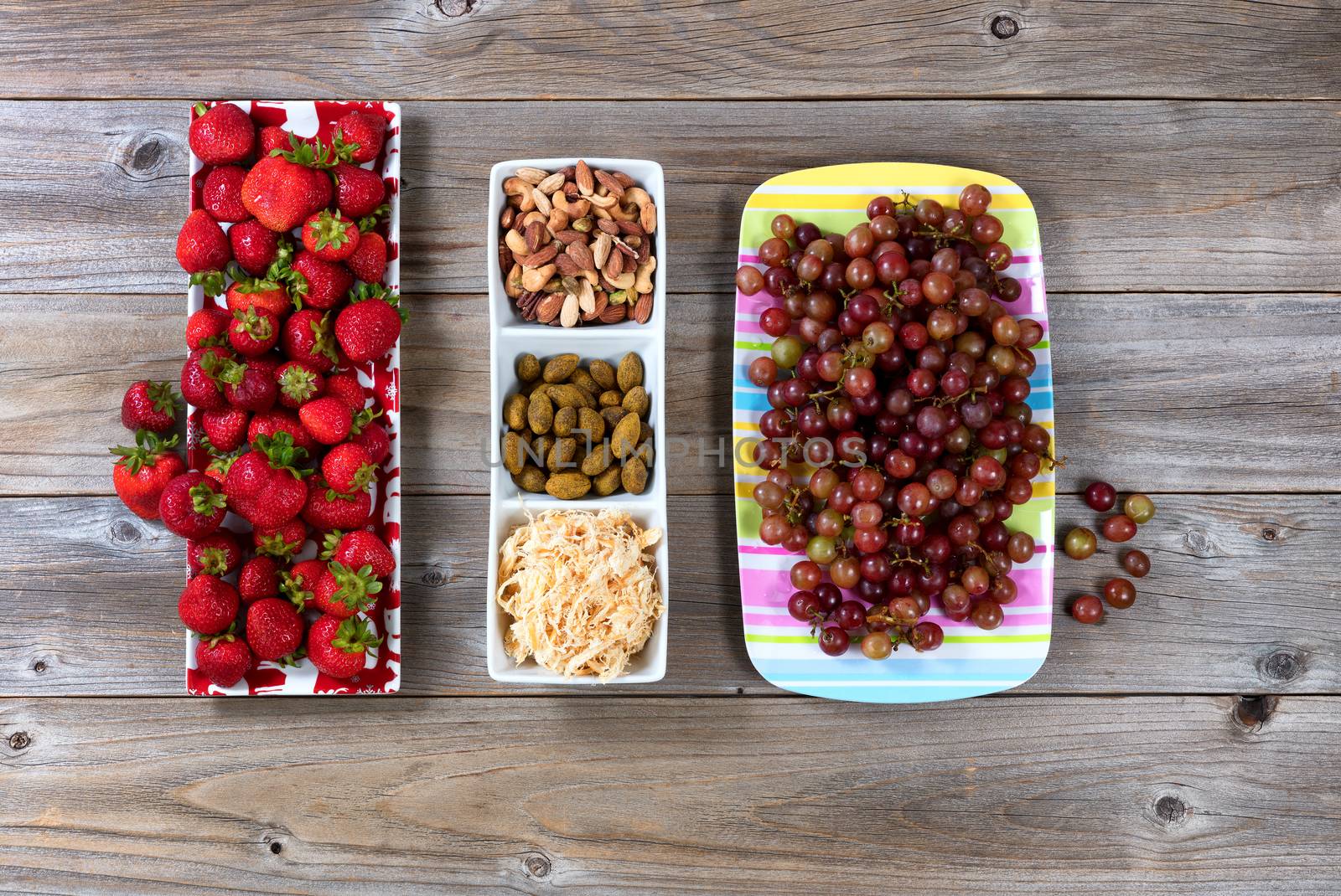 Fresh fruit, nuts and dried fish for healthy snacks. Flat lay view on rustic wood.