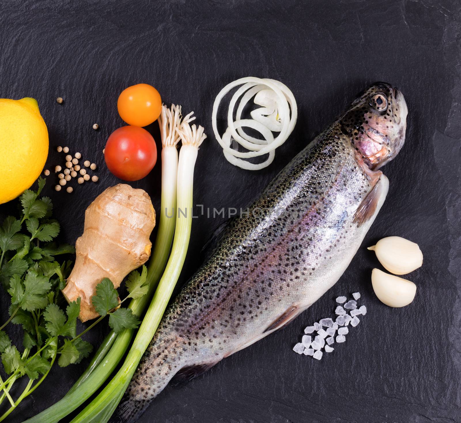 Overhead view of whole fish with various herbs, vegetables, and spices on black natural state. Healthy food concept. 