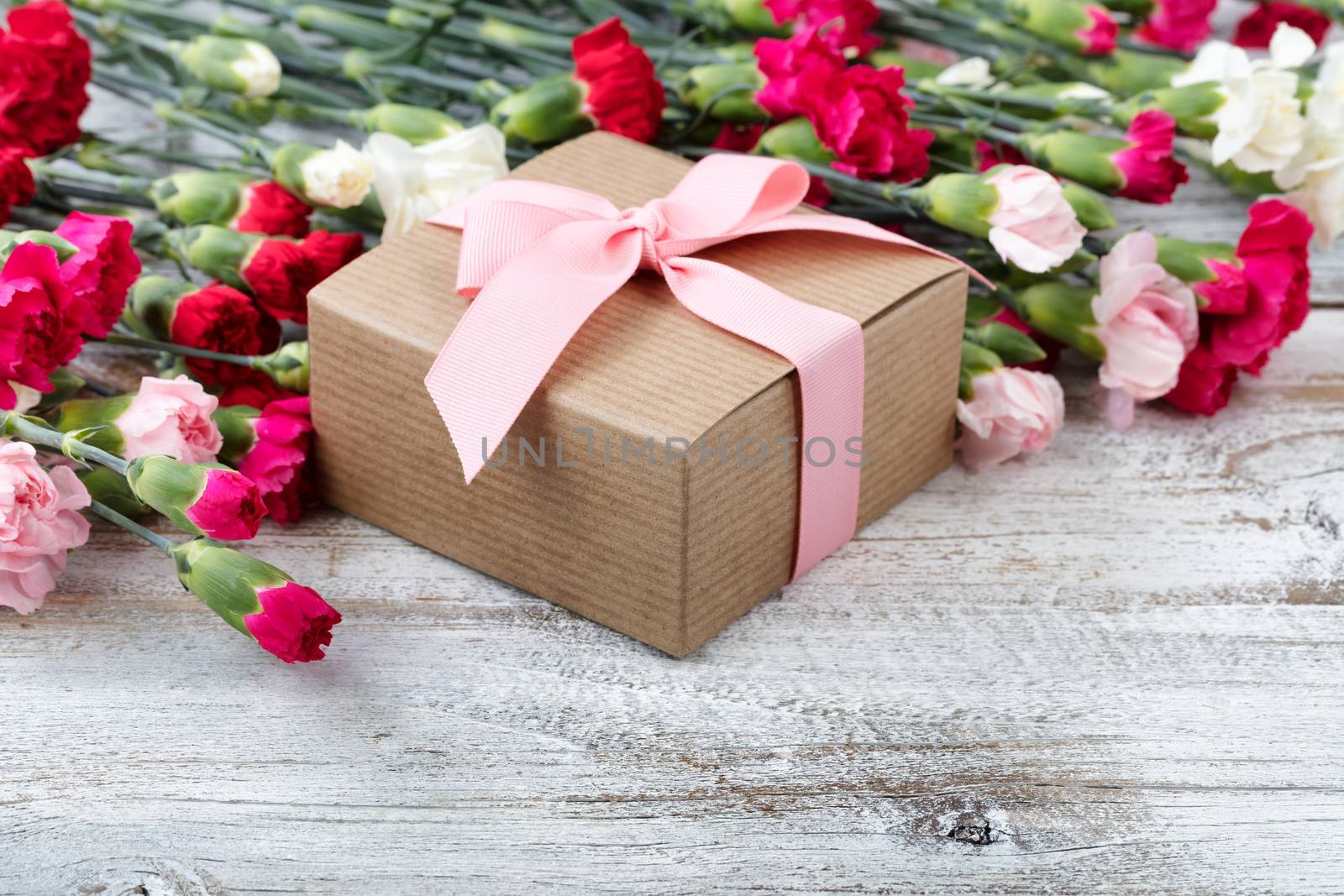 Gift box with colorful carnations in background on white weathered wooden boards 