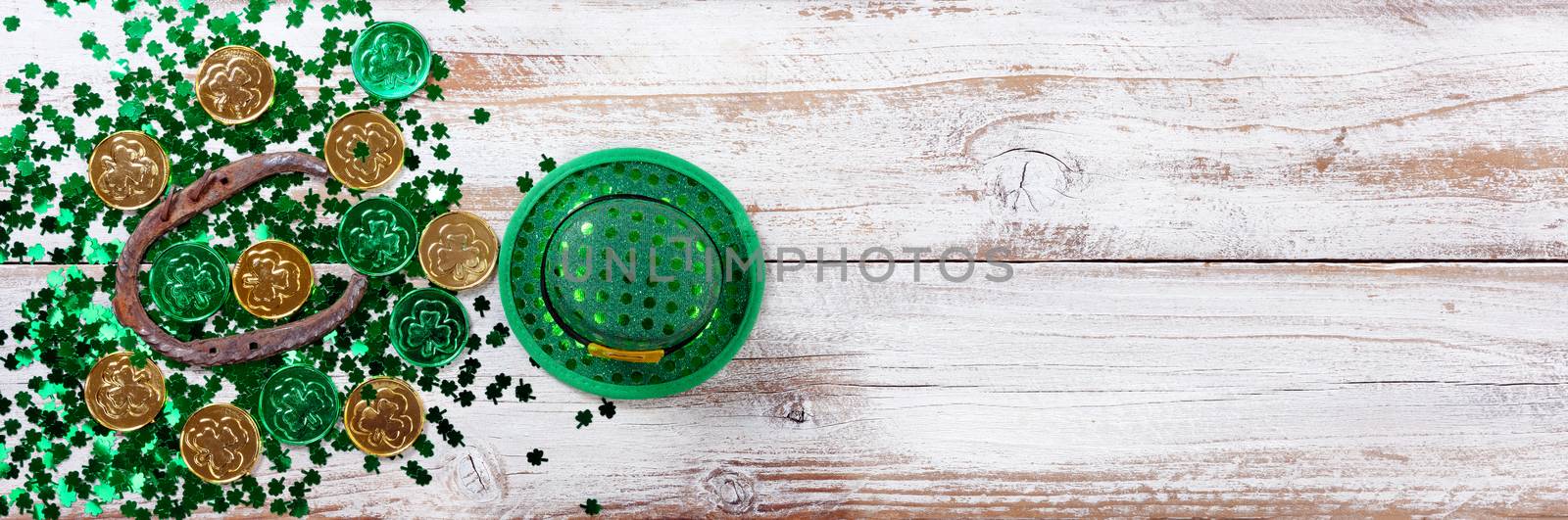 Bright green shamrock with gold coins, hat and rusty horseshoe for Saint Patrick Day on white rustic wooden background 