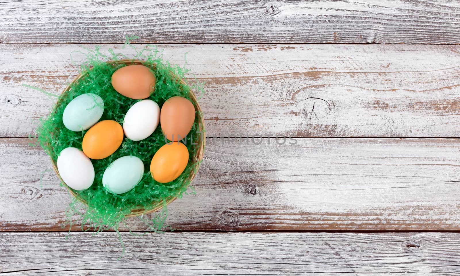 Real eggs in basket filled with green grass on rustic white wood by tab1962