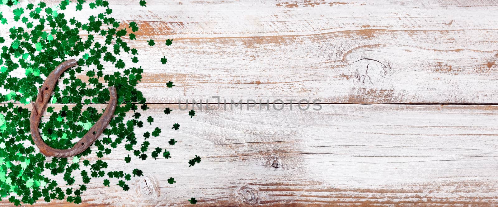 Bright green shamrock and rusty horseshoe for Saint Patrick Day on white rustic wooden background 