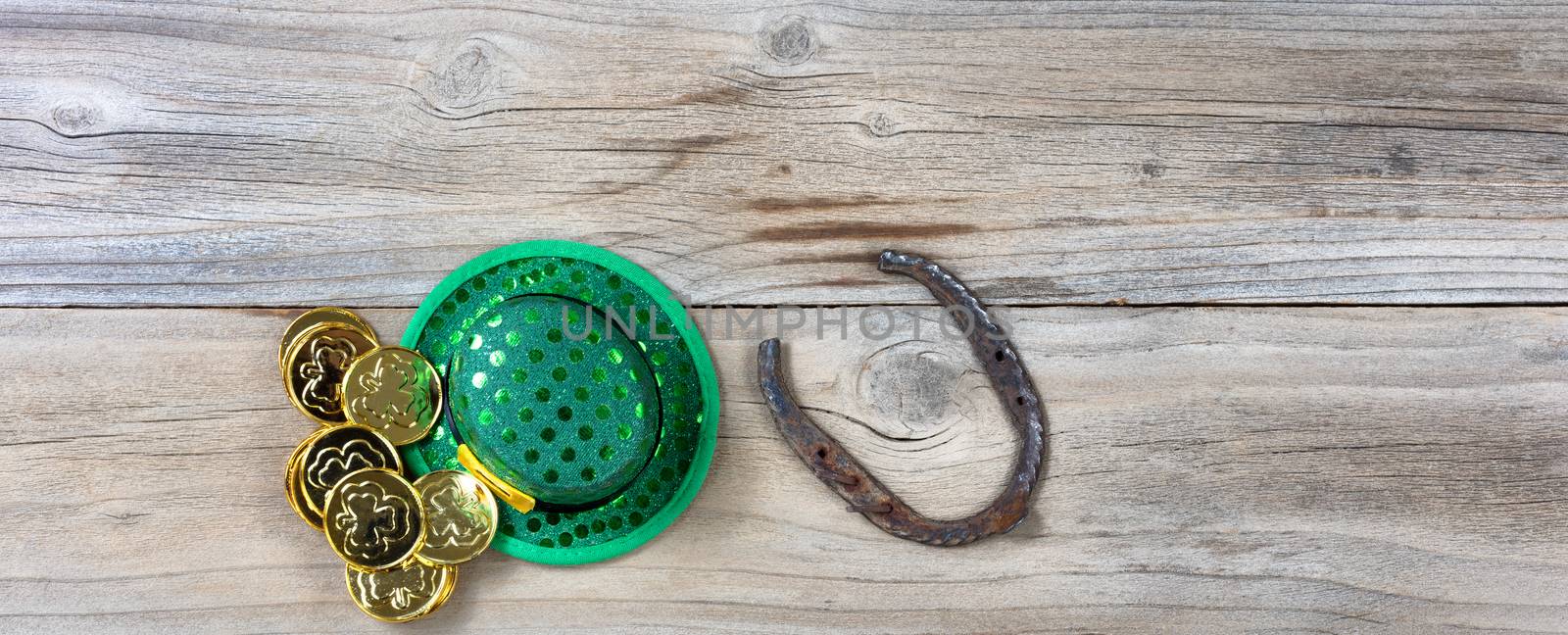 Lucky green hat, horseshoe and gold coins for St Patrick on rustic wooden boards in overhead view 