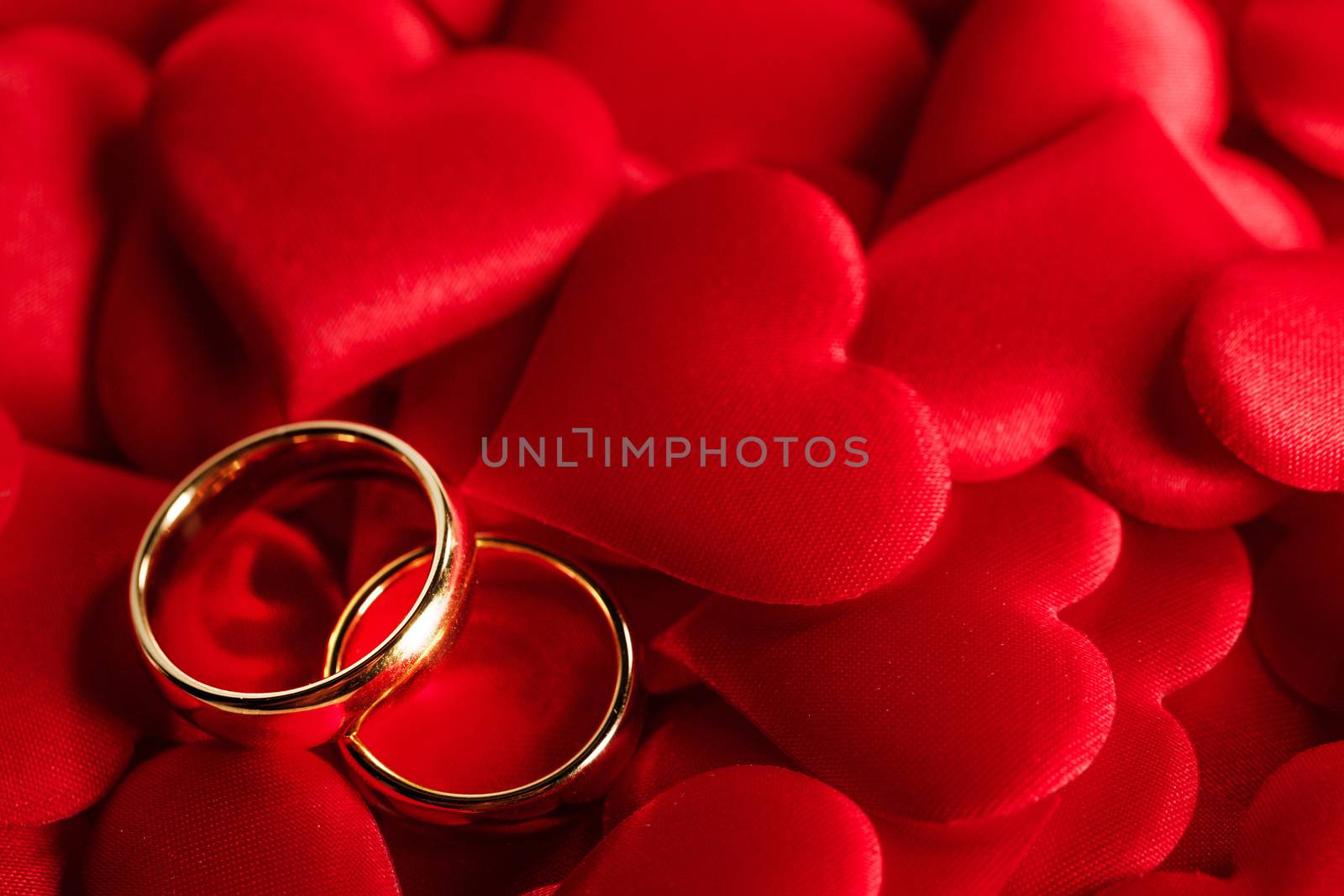 Two golden wedding rings on red satin hearts background