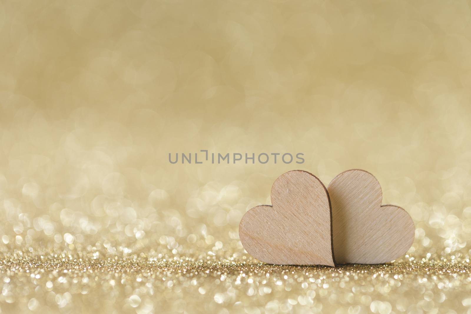Two small handmade wooden hearts on bright golden lights bokeh background Valentines day card