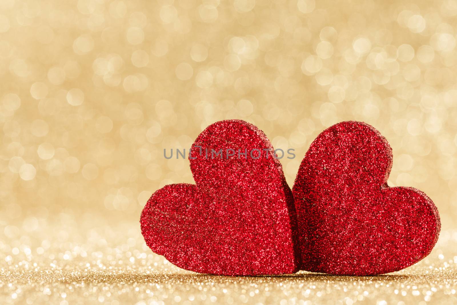 Two small handmade red glitter hearts on bright golden lights bokeh background Valentines day card