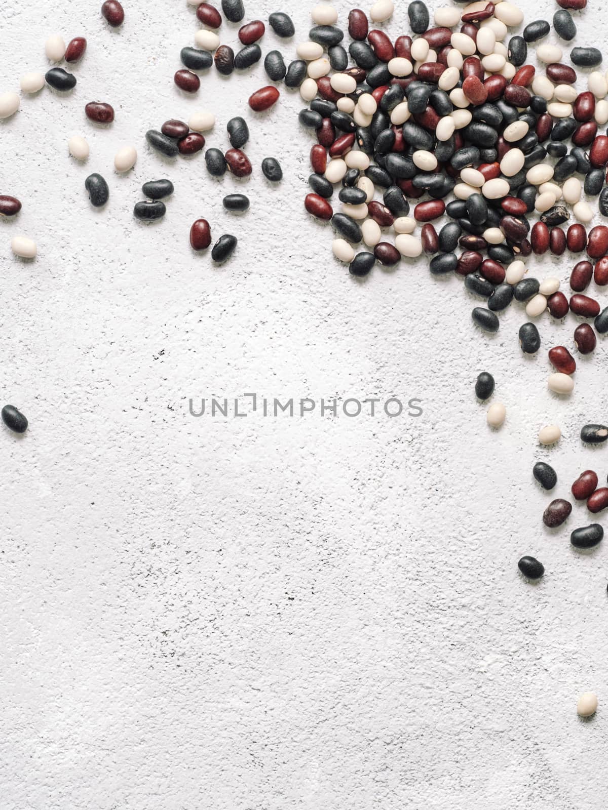 Top view of raw mixed beans on gray concrete background. Mixed of uncoocked black, red and white beans with copy space. Fodd background. Vegan protein concept.