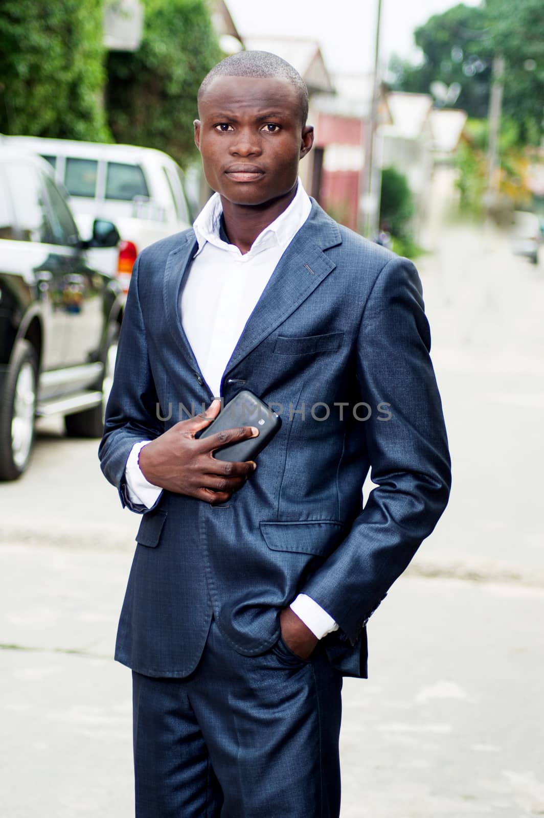 African businessman standing outside and holding his phone by vystek