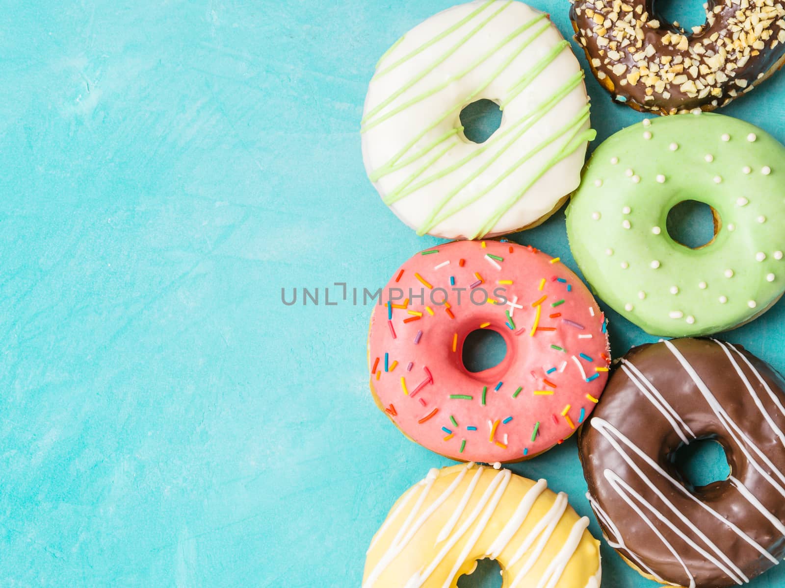 Top view of assorted donuts on blue concrete background with copy space. Colorful donuts background. Various glazed doughnuts with sprinkles.