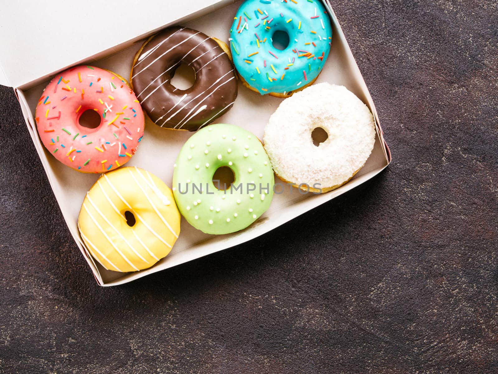 Top view of paper box with colorful donuts on dark cement background. Copy space.
