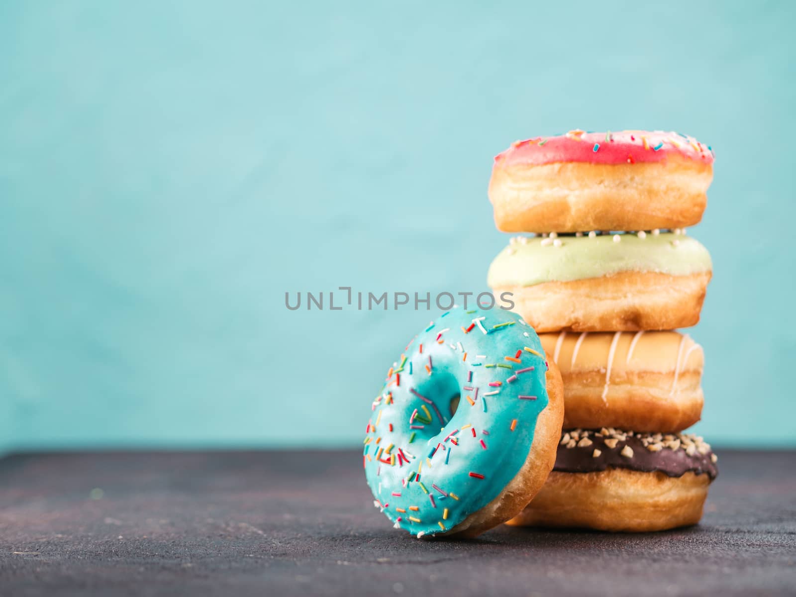 Stack of assorted donuts on black and blue cement background. Blue glazed doughnut with sprinkles on foreground. Copy space. Shallow DOF