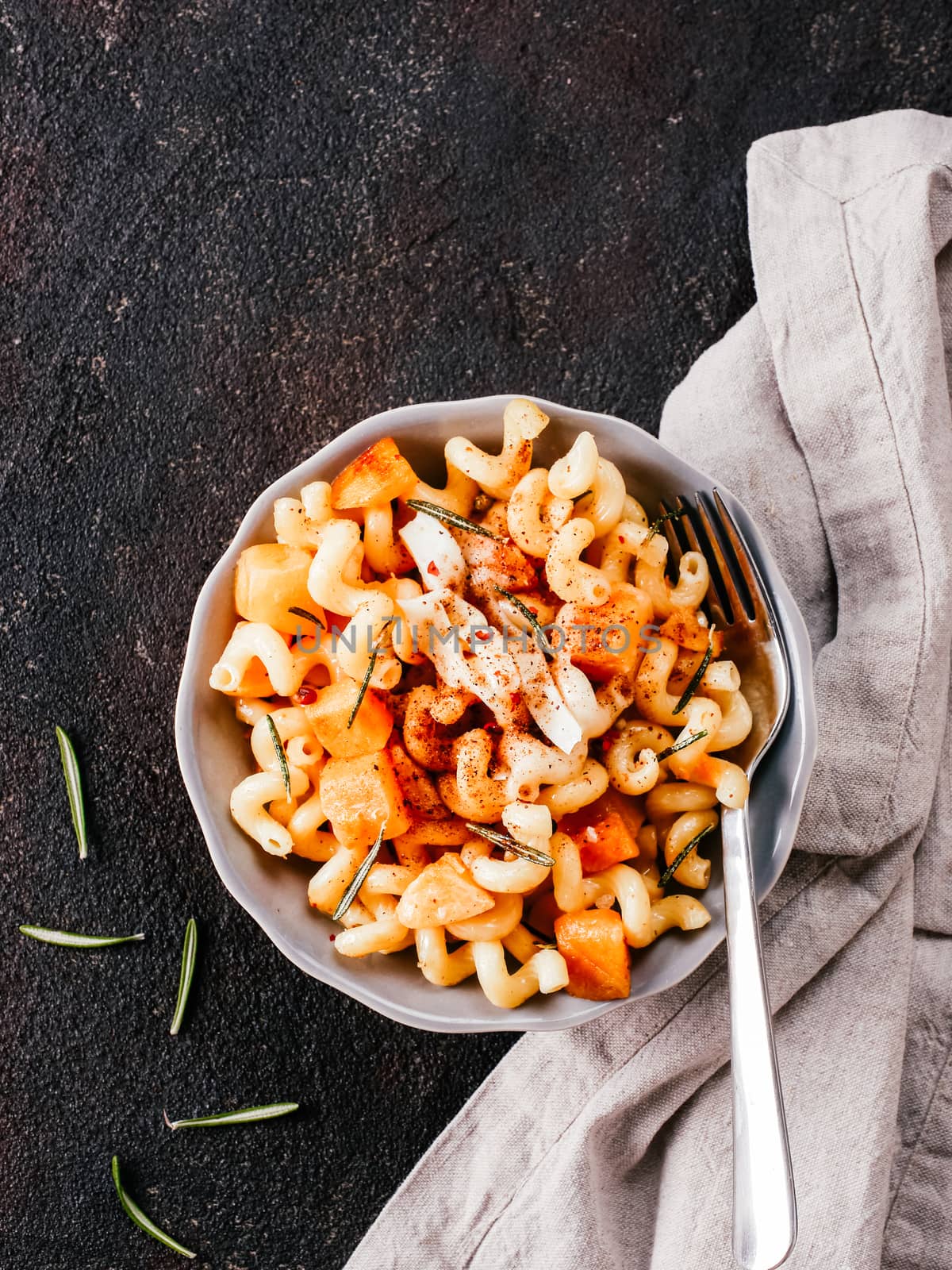 Fusilli pasta with pumpkin, rosemary and brie cheese. Idea recipe pasta. Vegetarian food. Homemade pasta dish in gray bowl over black concrete background. Copy space. Top view or flat lay.