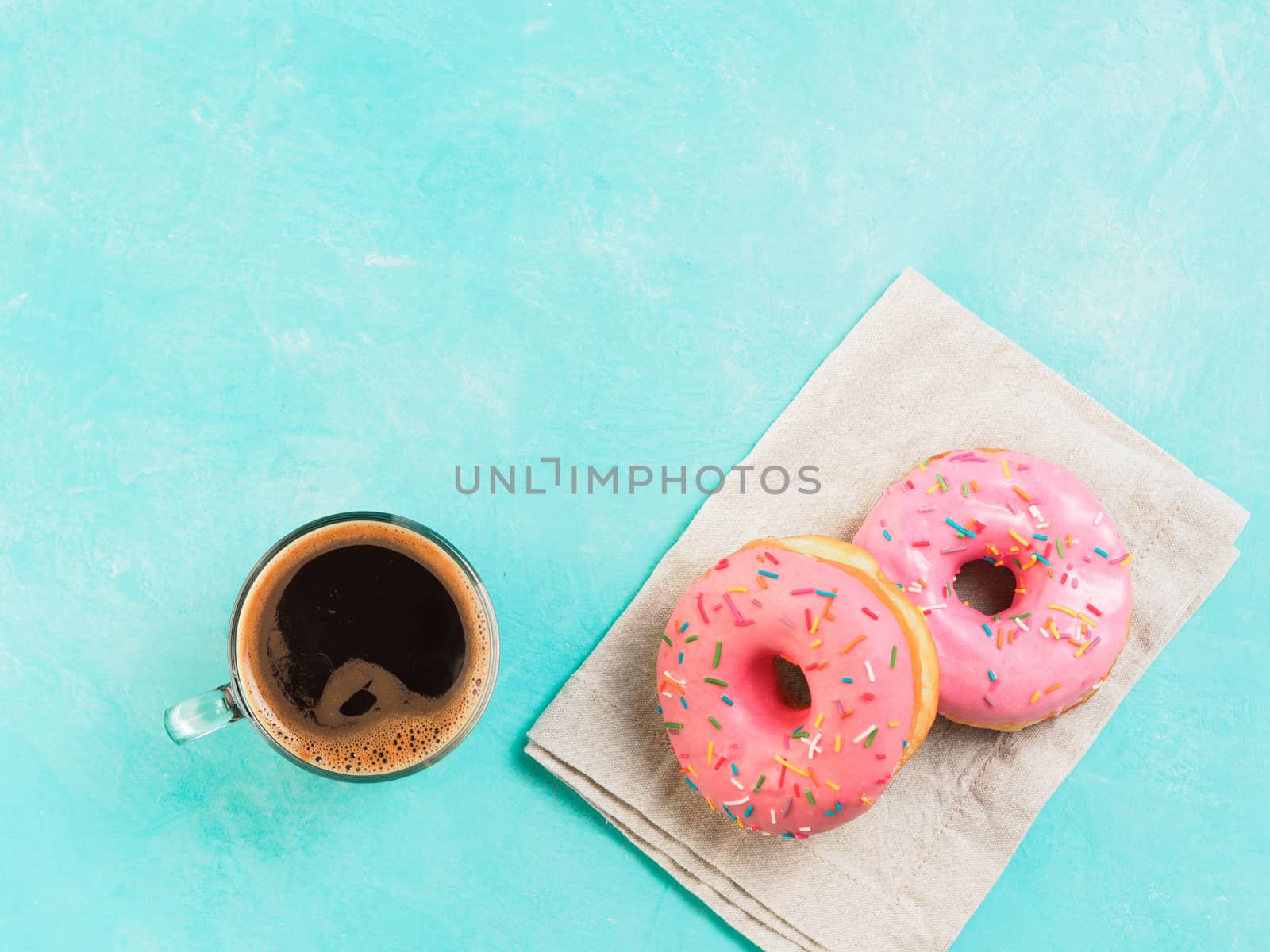 Top view of two pink donuts and coffee on blue concrete background with copy space. Colorful donuts and coffee cup with copyspace. Glazed doughnuts with sprinkles