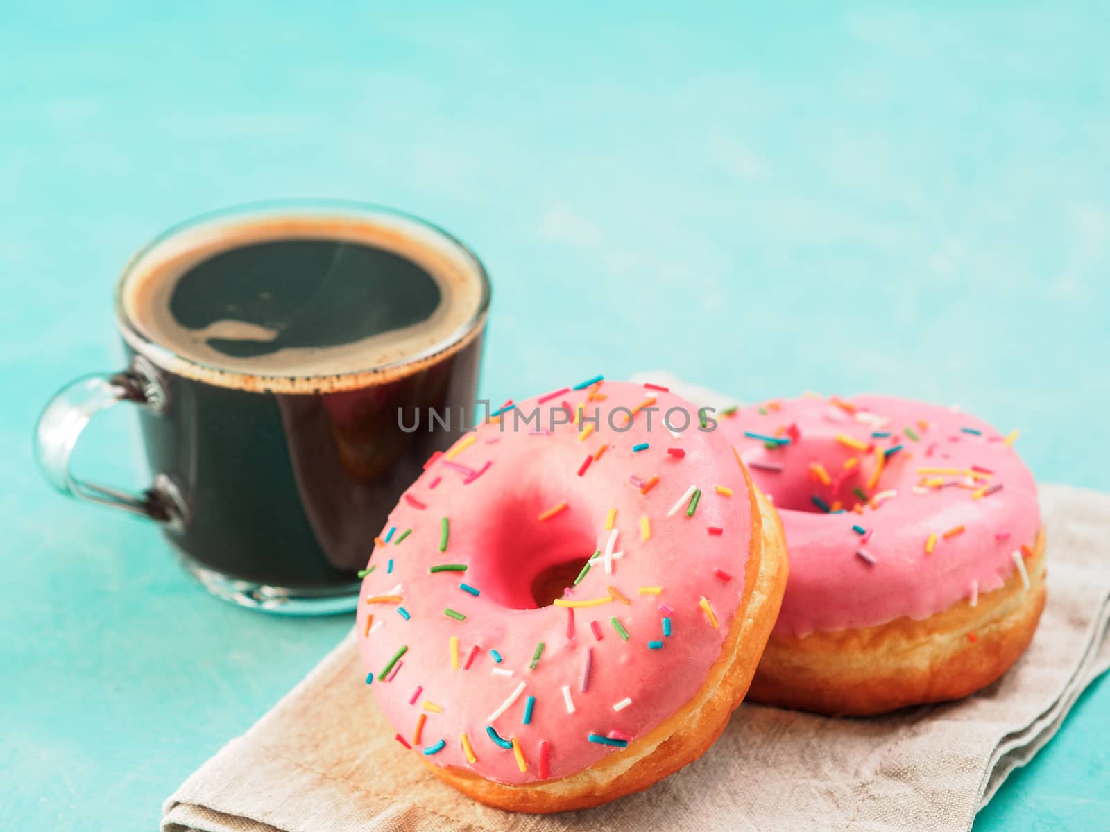 Two pink donuts and coffee on blue concrete background with copy space. Colorful donuts and coffee cup with copyspace. Glazed doughnuts with sprinkles