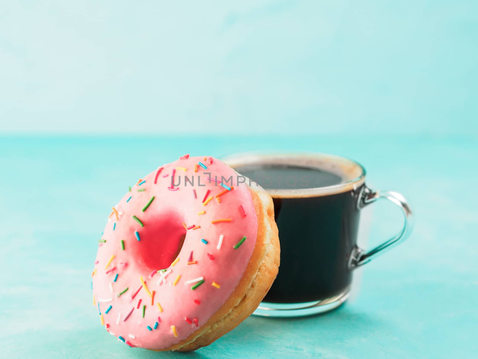 Pink donut and coffee on blue concrete background with copy space. Glazed doughnut and coffee cup with copyspace