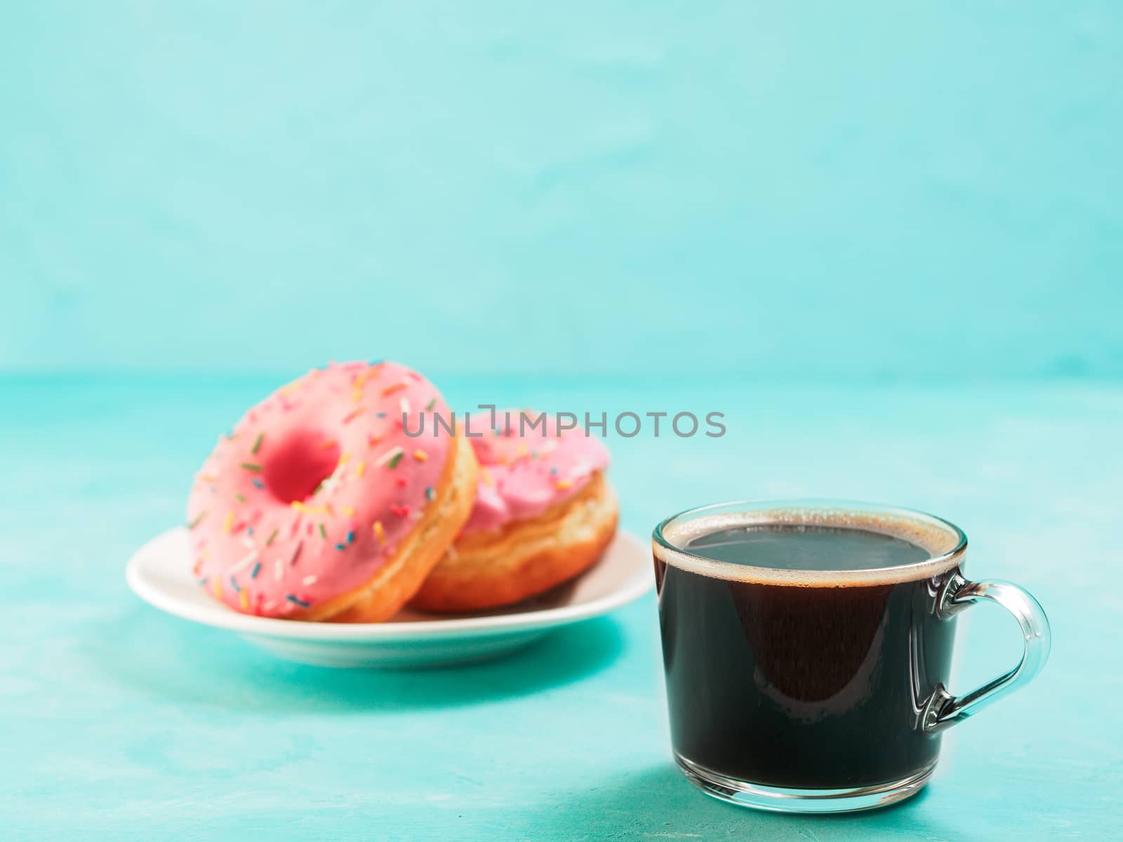 Two pink donuts and coffee on blue concrete background with copy space. Colorful donuts in plate and coffee cup with copyspace. Glazed doughnuts with sprinkles