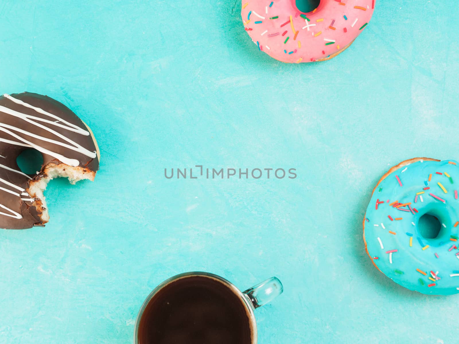Top view of assorted donuts and coffee on blue concrete background with copy space. Colorful donuts and coffee background. Various glazed doughnuts with sprinkles.