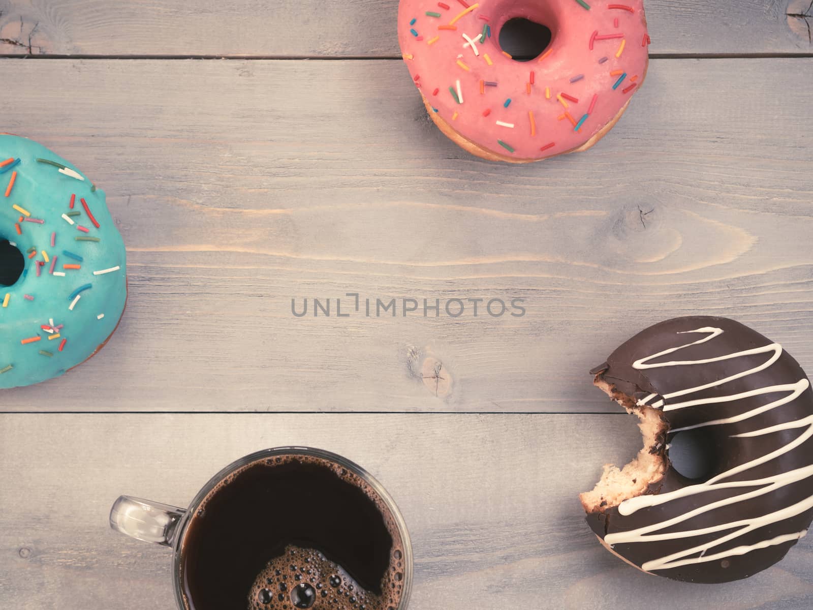 Top view of assorted donuts and coffee on gray wooden background with copy space. Colorful donuts and coffee with copyspace. Various glazed doughnuts with sprinkles on grey wooden table. Toned image