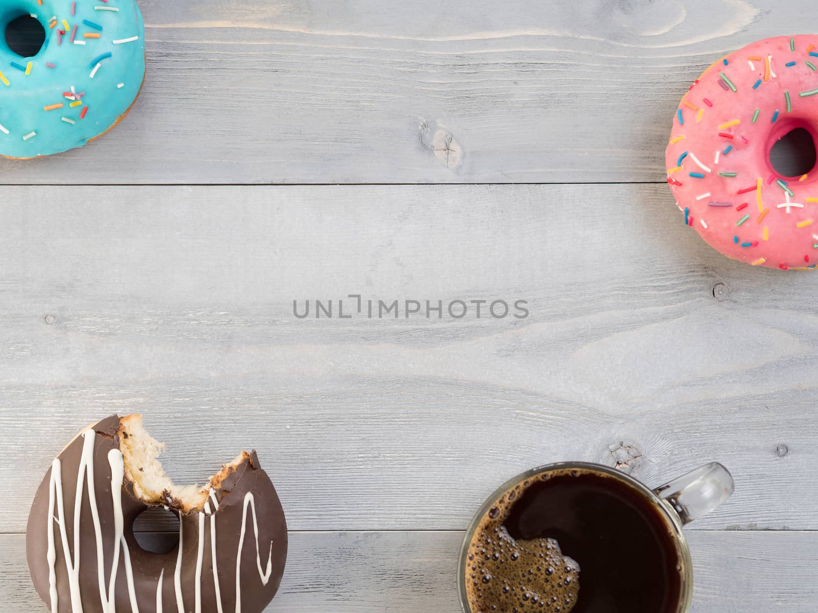 Top view of assorted donuts and coffee on gray wooden background with copy space. Colorful donuts and coffee background with copyspace. Various glazed doughnuts with sprinkles on grey wooden table.