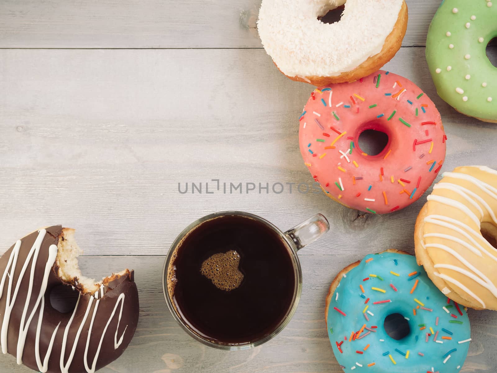 Top view of assorted donuts and coffee on gray wooden background with copy space. Colorful donuts and coffee with copyspace. Various glazed doughnuts with sprinkles on grey wooden table. Toned image
