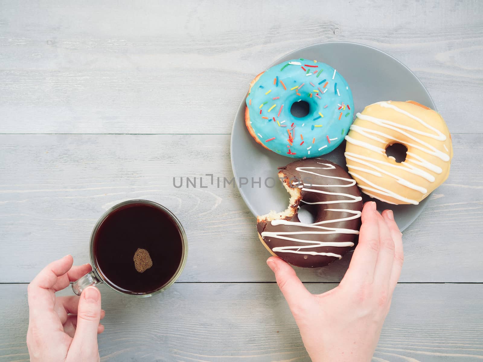 Woman hands with coffee and assorted donuts over gray wooden table. Top view of colorful donuts and coffee on grey wooden background.