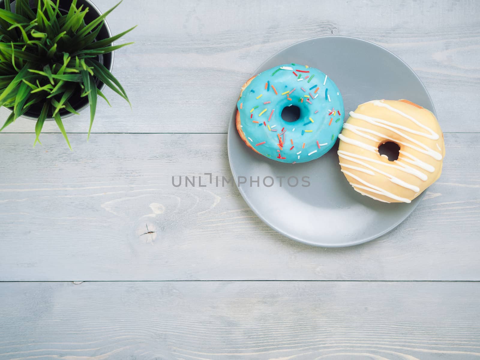 Top view of two donuts on gray wooden background with copy space. Colorful donuts on plate with copyspace. Glazed doughnuts with sprinkles on grey wooden table. Smile sign, good morning concept