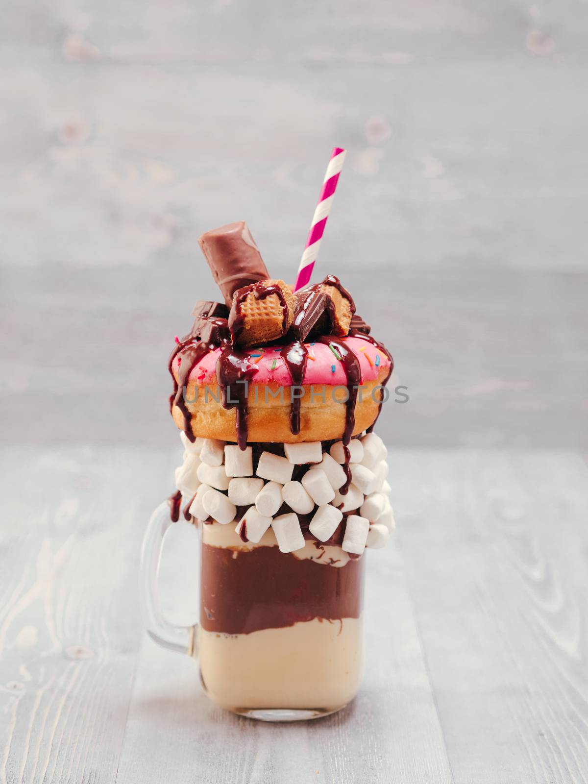 Chocolate and donuts extreme milkshake with marshmallow and other sweets in mason jar on gray wooden background. Crazy freakshake on gray wooden table with copy space