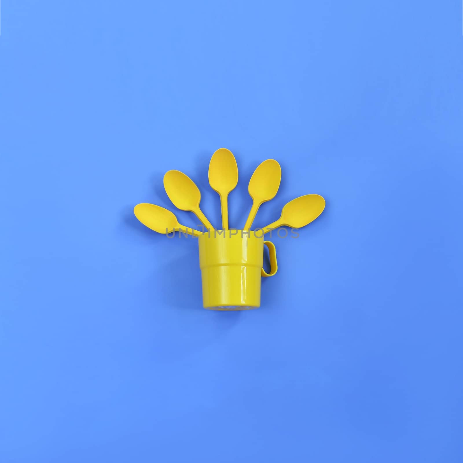 A yellow plastic mug and spoons lay in it on a bright blue background. The concept of a holiday, a picnic