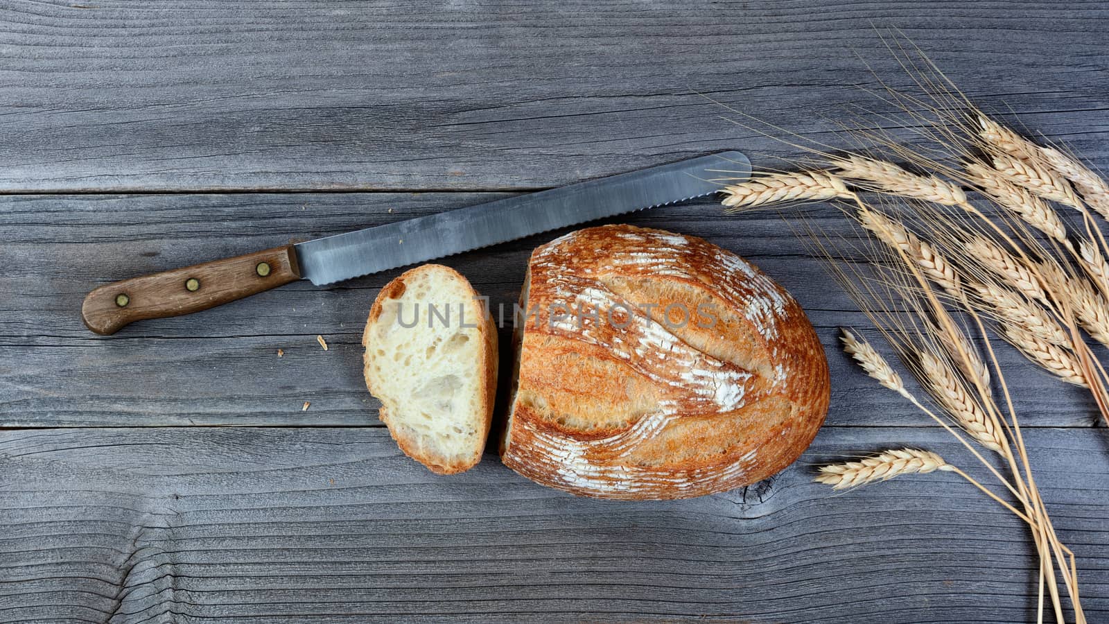 whole loaf of bread with cutting knife and stalks on rustic wood by tab1962