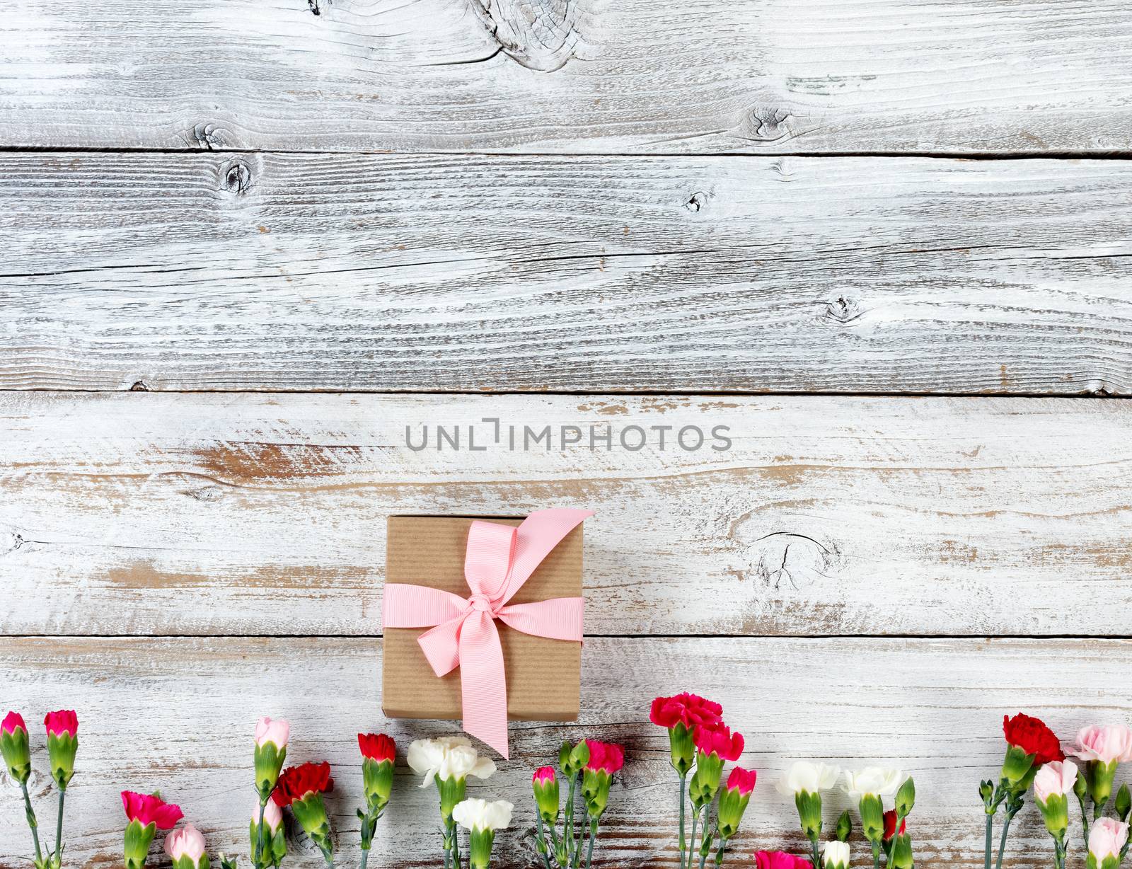 Colorful carnations and gift forming bottom border on white weathered wooden boards 