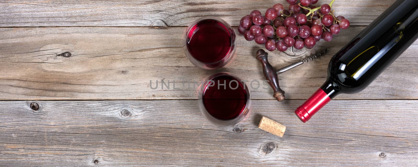Unopen bottle of red wine and glasses with grapes on rustic wood by tab1962