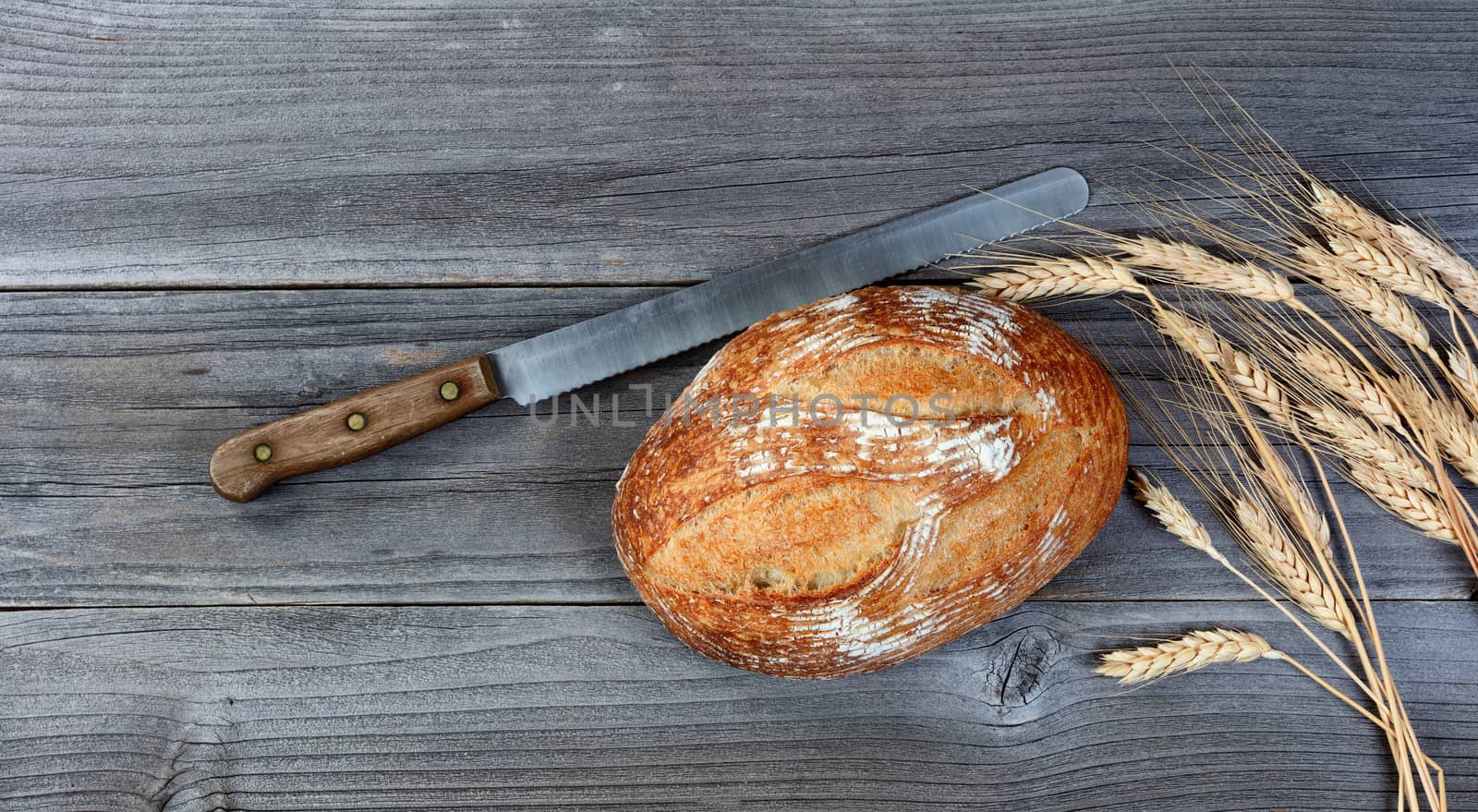 Baked whole wheat loaf of bread with cutting knife and stalks on by tab1962
