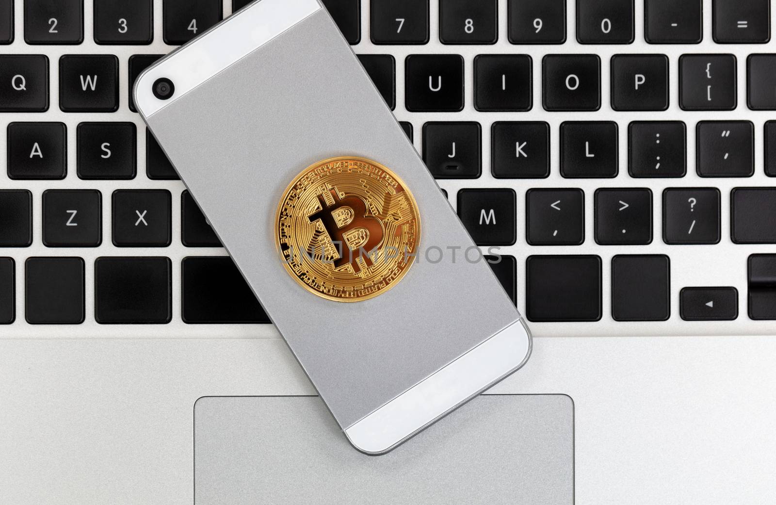 Bitcoin currency on smart phone with computer keyboard in background.  Crypto investment via wireless mobile technology concept
