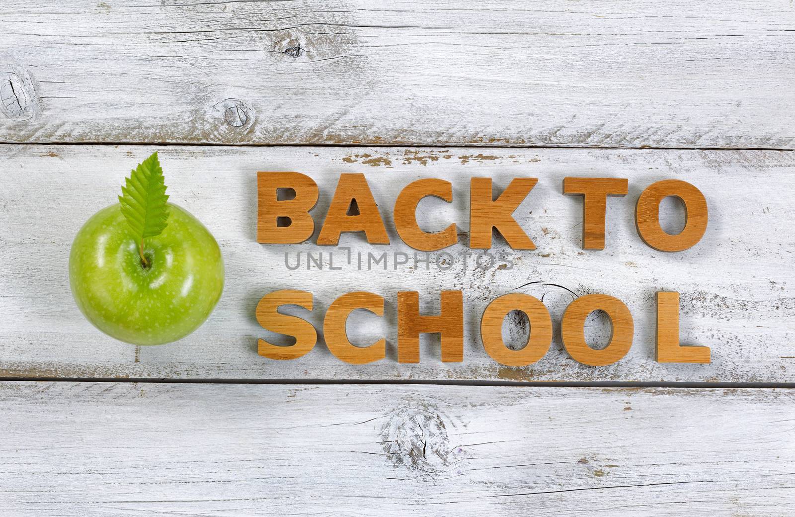 Wooden letters spelling back to school and green apple on top of rustic white boards.