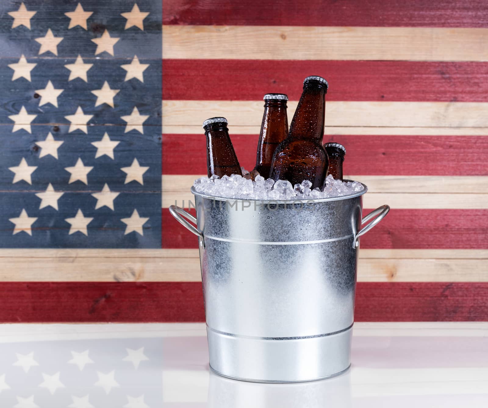 A bucket of cold bottled beer on ice with USA wooden flag in background. 