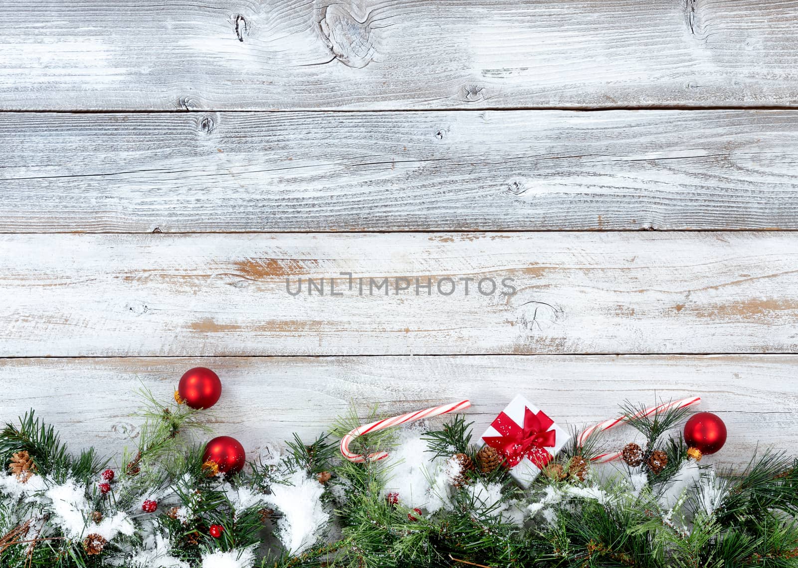 Bottom border of Christmas snow covered evergreen branches with other holiday decorations on white rustic wood