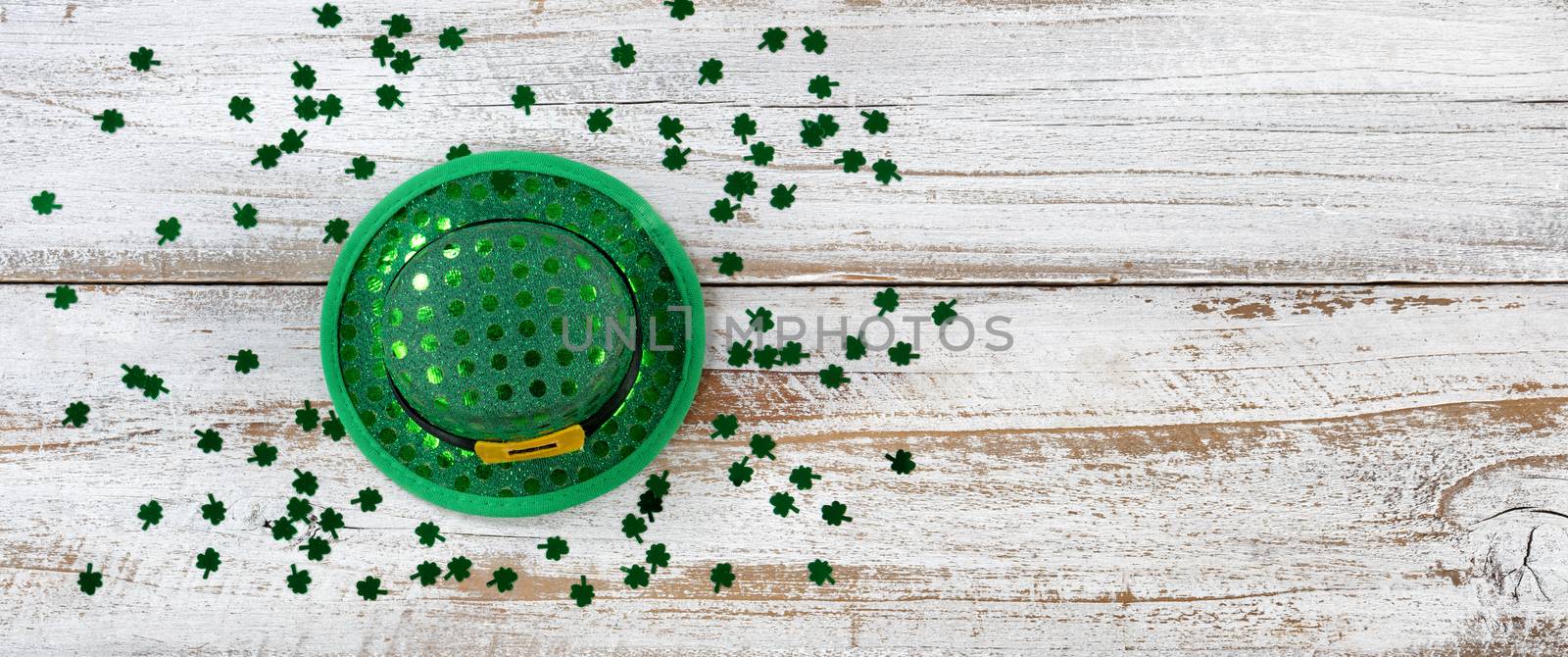 St Patrick day good luck hat with shiny clovers on rustic white wooden boards in overhead view 