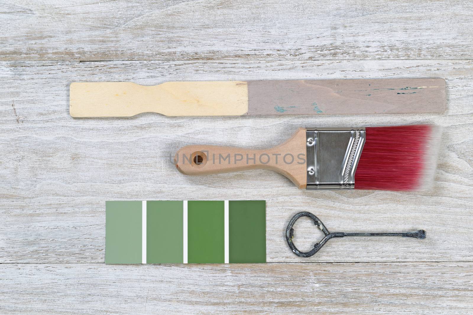 Paint brush with used stick, lid opener, and paint color choice on old white wooden boards