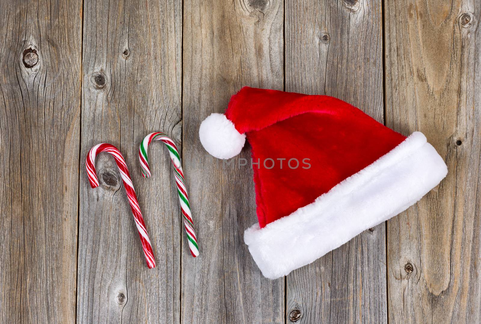 Traditional Christmas Santa cap and candy canes on rustic wood. Boards in vertical pattern.  