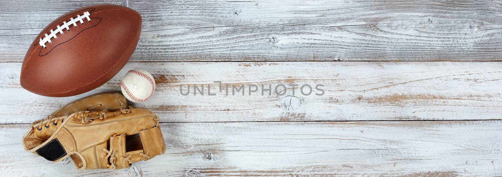 American football and baseball with mitt on white rustic wood