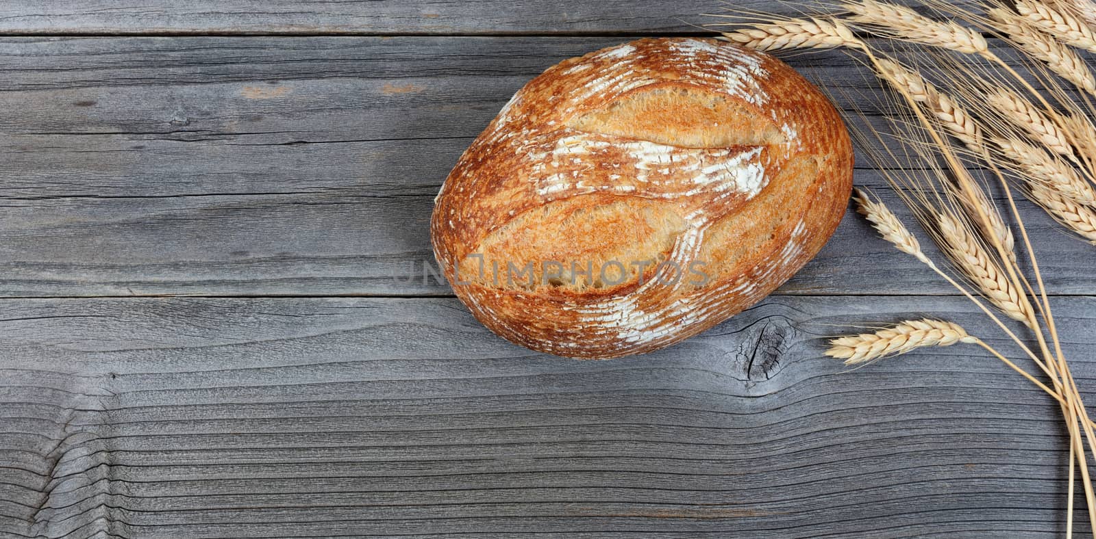 Overhead view of baked whole loaf of bread and wheat stalks on rustic wooden boards