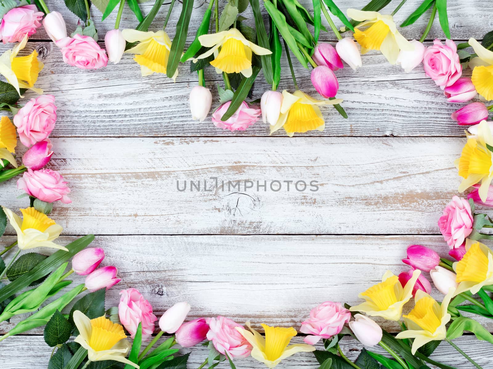 Assortment of spring flowers forming heart shape on white rustic wooden boards 