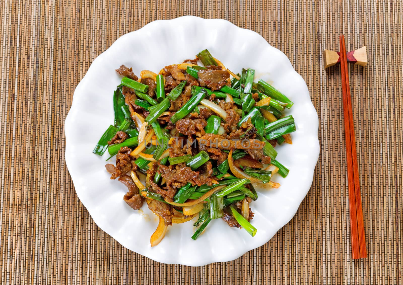 Top view of beef and green onions in white plate with bamboo mat underneath.  