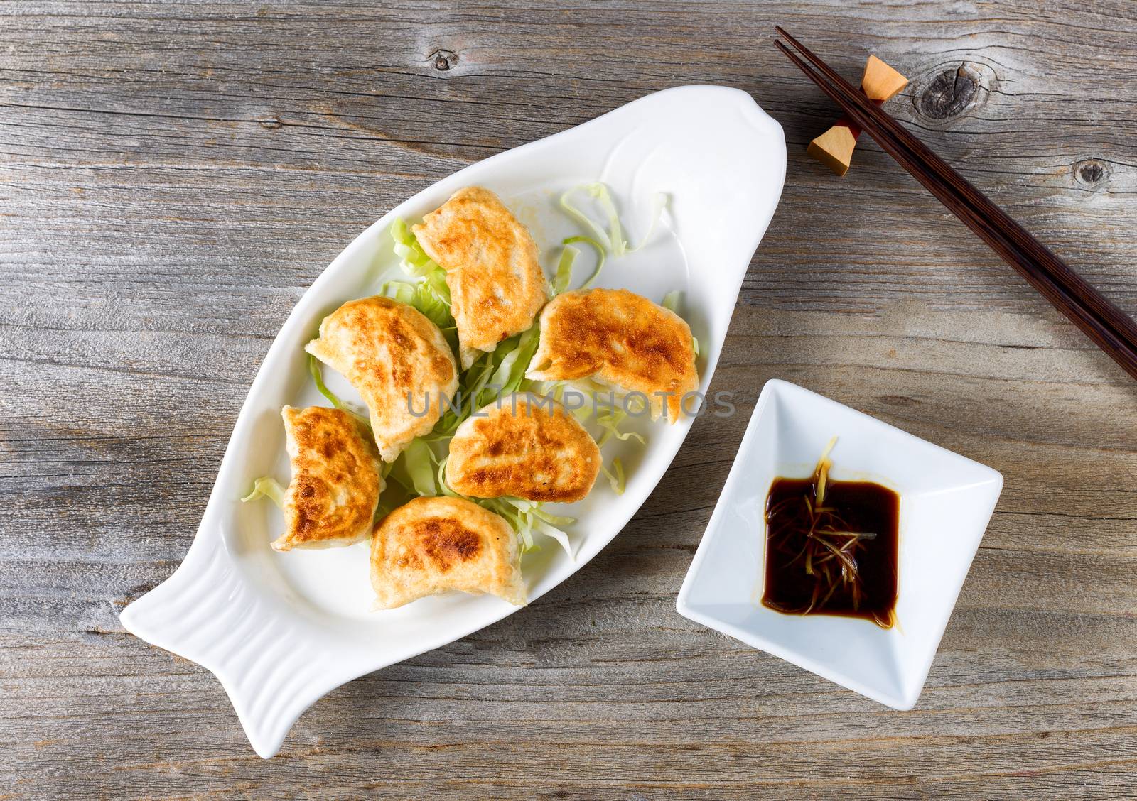 High angled view of Chinese dumpling with sauce in bowl with chopsticks on rustic wood. 