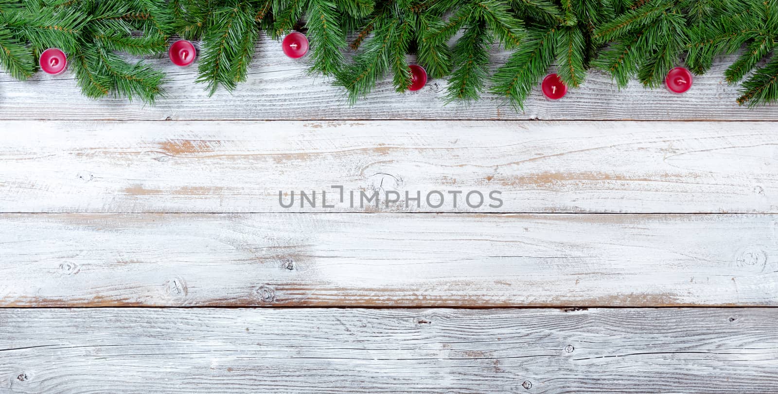 Top border of Christmas evergreen branches and red candles on white vintage wood