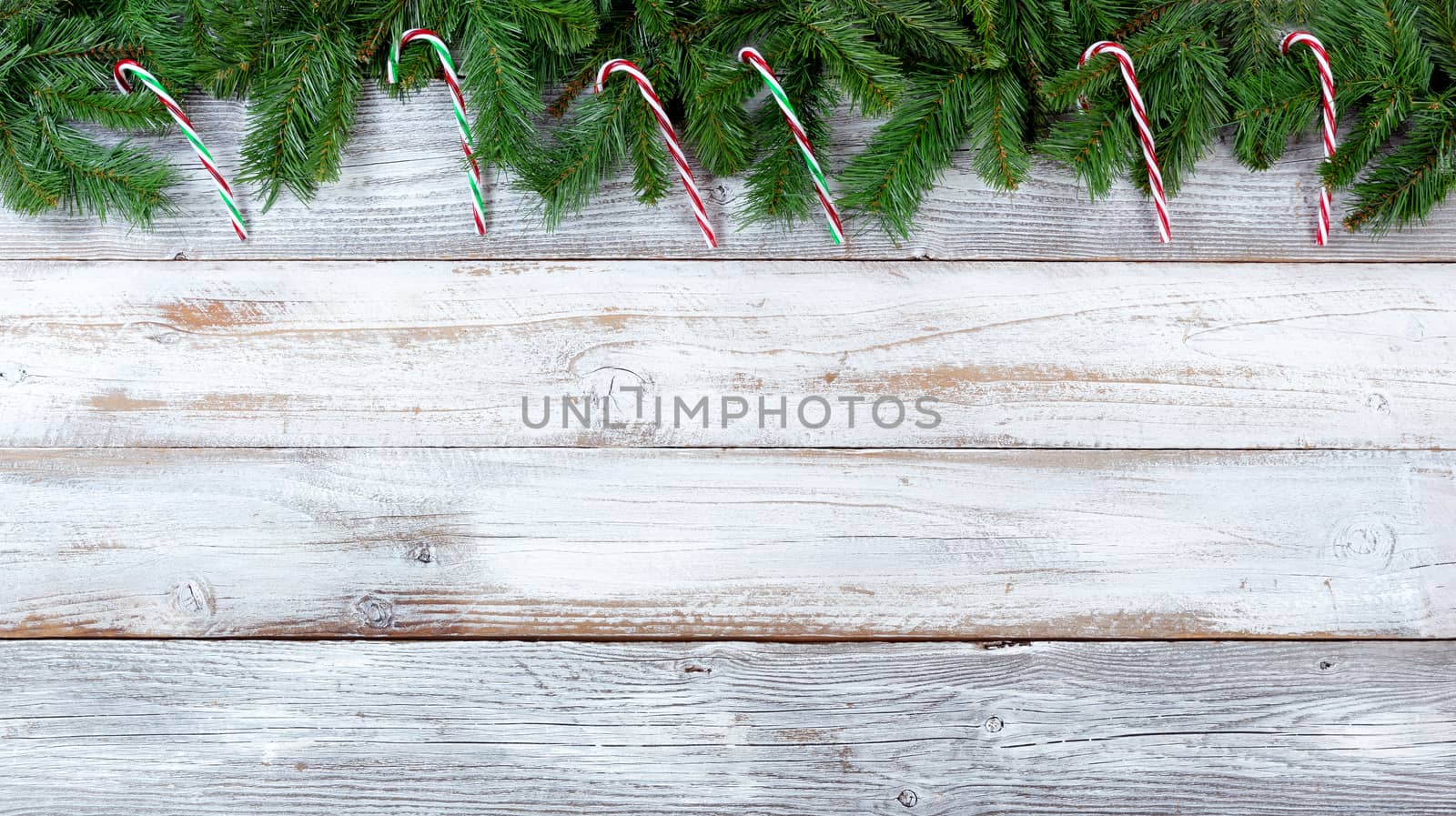Top border of Christmas evergreen branches and candy canes on white vintage wood